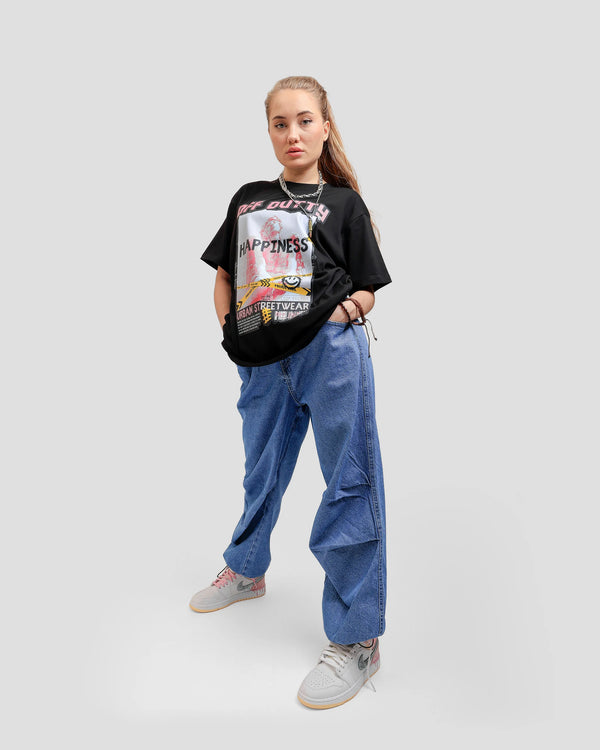 Front photo of a female Russian model in a dynamic pose wit her hands in her pockets, wearing Off Dutty's 'What Is Happiness' black relaxed t-shirt from Off Dutty's 'Rare and Radiant' collection, paired with a blue jeans and Air Jordan 1 mid paint drip sneaker. She complements her look with a chain necklace and some bracelets.
