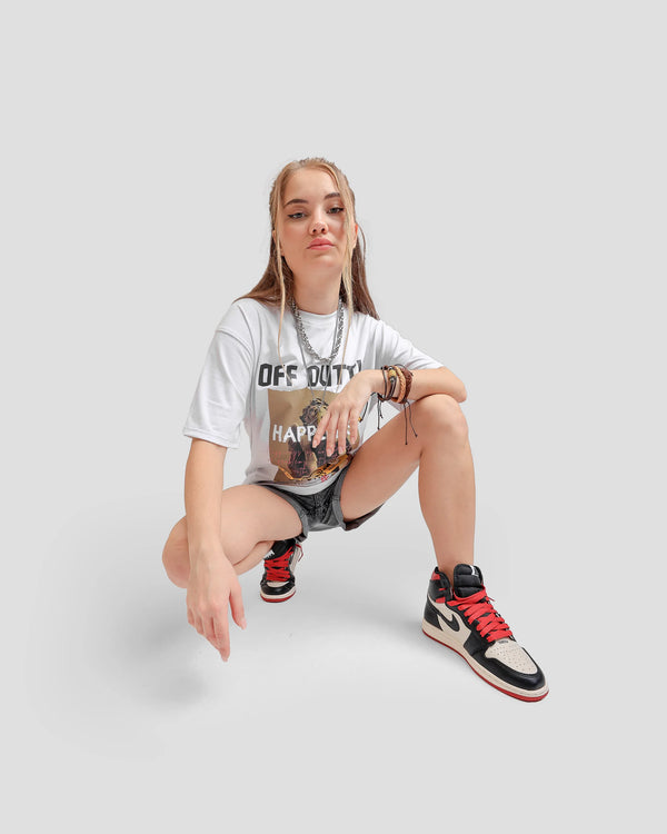 Front photo of a  female Russian model in a dynamic pose, wearing Off Dutty's 'What Is Happiness' white relaxed t-shirt paired with a black  jeans short and Air Jordan 1 Retro High OG NRG 'Not For Resale' sneaker. She complements her look with a chain necklace and some bracelets on her left hand. 