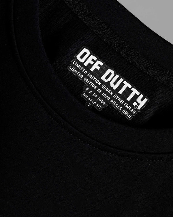 Close-up of the inside label of Off Dutty's 'Embracing Your Presence' black relaxed t-shirt, showcasing the printed Off Dutty logo and 'Limited Edition Urban Streetwear' text. The label also highlights the t-shirt's unique number in the limited series of 1000, its 'Relaxed Fit' designation, and the size of the garment.